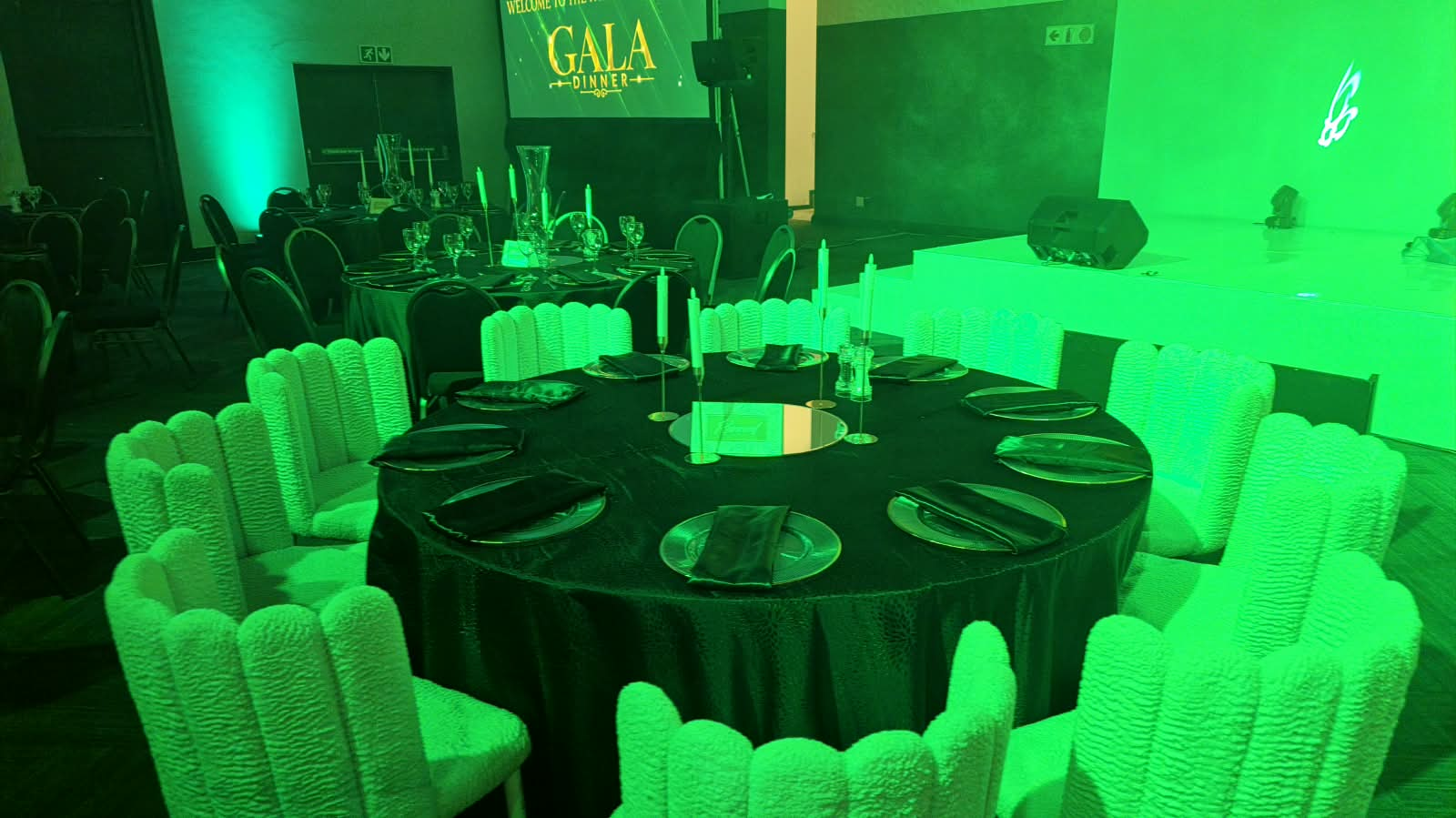Gala dinner table under green uplighting with candelabras and draped chairs
