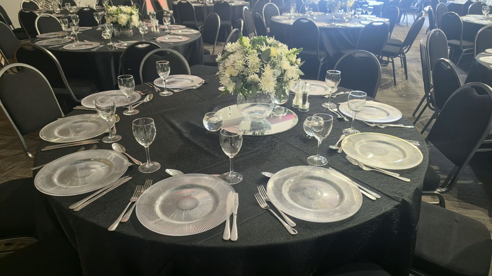 Round table set with charger plates, glassware and a white floral centrepiece